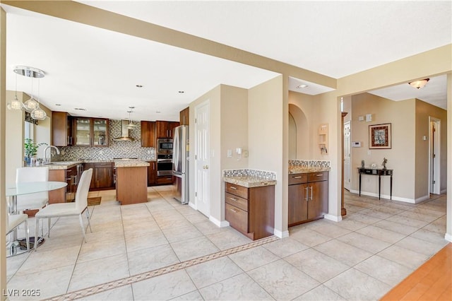 8416 Dry Cliff Cir, Las Vegas, NV 89128 - kitchen featuring wall chimney range hood, appliances with stainless steel finishes, a center island, tasteful backsplash, and arched walkways