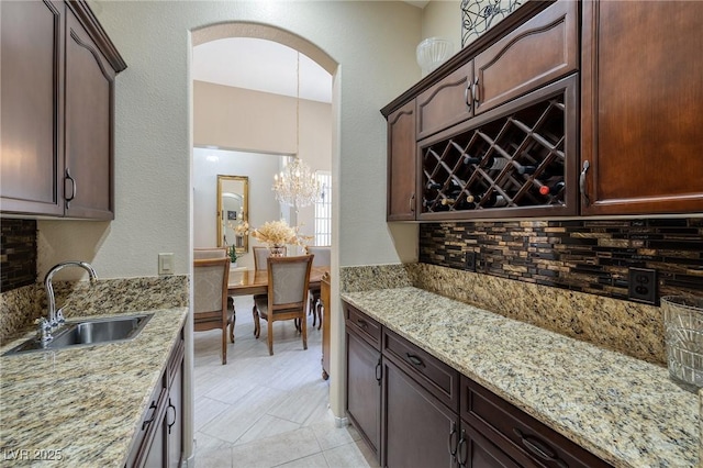 1329 Calle Cantar, Henderson, NV 89012 - kitchen featuring backsplash, light stone countertops, a chandelier, arched walkways, and dark brown cabinetry