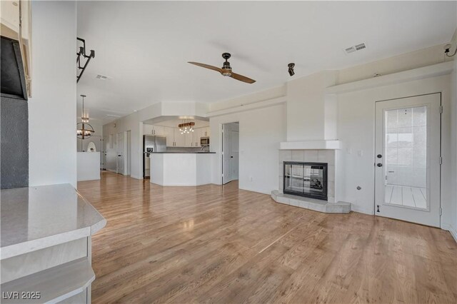 483 Marina Cv, Boulder City, NV 89005 - unfurnished living room featuring a chandelier, a ceiling fan, a tile fireplace, and light wood-style floors