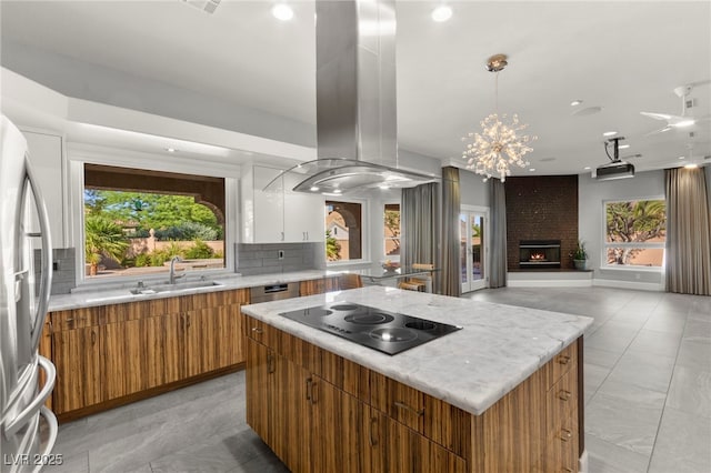 5680 N Fort Apache Rd, Las Vegas, NV 89149 - kitchen with island range hood, black electric stovetop, brown cabinetry, a kitchen island, and tasteful backsplash