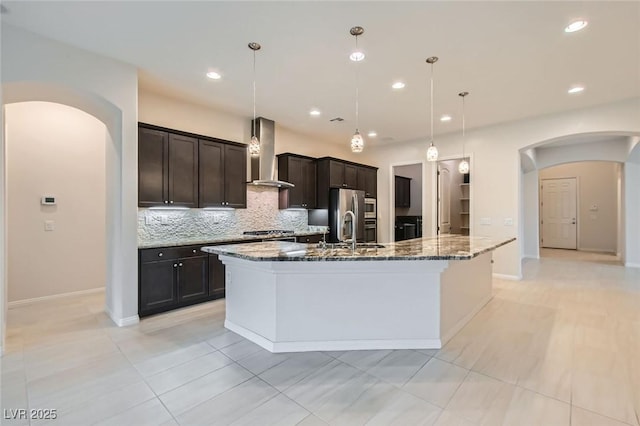 8732 Kendall Brook Cir, Las Vegas, NV 89149 - kitchen with arched walkways, wall chimney exhaust hood, tasteful backsplash, a spacious island, and dark brown cabinetry