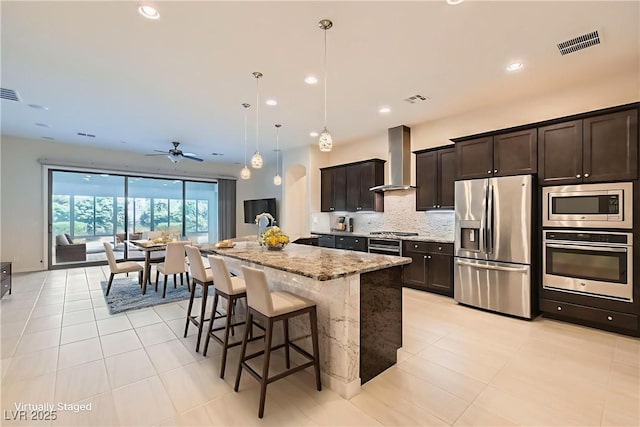 8732 Kendall Brook Cir, Las Vegas, NV 89149 - kitchen featuring stainless steel appliances, wall chimney exhaust hood, light stone countertops, dark brown cabinetry, and recessed lighting