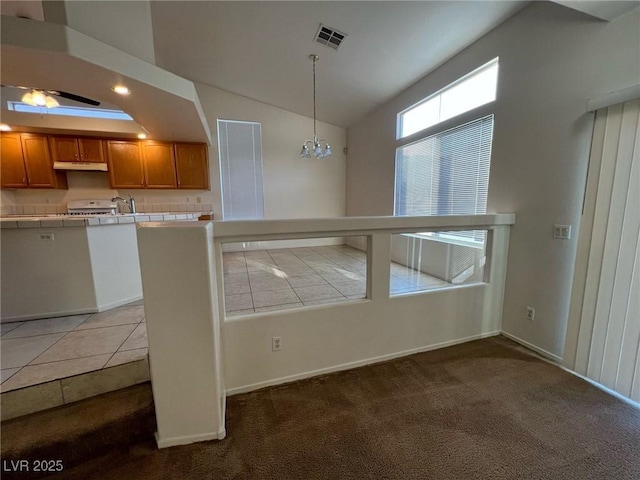8704 Autumn Wreath Ave, Las Vegas, NV 89129 - kitchen featuring tile countertops, under cabinet range hood, brown cabinets, carpet floors, and vaulted ceiling