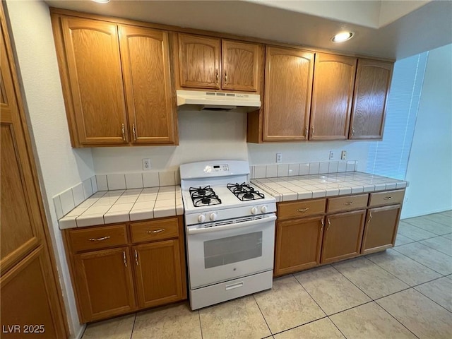 8704 Autumn Wreath Ave, Las Vegas, NV 89129 - kitchen with white gas range oven, under cabinet range hood, tile counters, light tile patterned floors, and recessed lighting