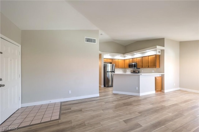 370 Manti Pl Unit 21, Henderson, NV 89014 - kitchen with appliances with stainless steel finishes, light wood-style floors, brown cabinetry, vaulted ceiling, and light countertops