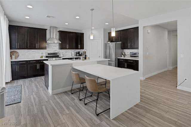 7890 S Miller Ln, Las Vegas, NV 89113 - kitchen featuring wall chimney range hood, stainless steel appliances, backsplash, a kitchen bar, and light countertops