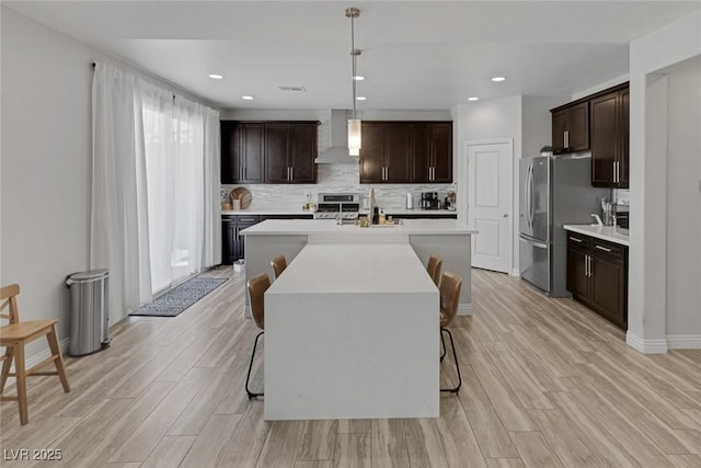 7890 S Miller Ln, Las Vegas, NV 89113 - kitchen featuring wall chimney range hood, stainless steel appliances, light countertops, backsplash, and a kitchen island with sink