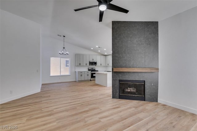 6126 Bedrock Ct, North Las Vegas, NV 89031 - unfurnished living room featuring ceiling fan, a tile fireplace, light wood finished floors, high vaulted ceiling, and a chandelier