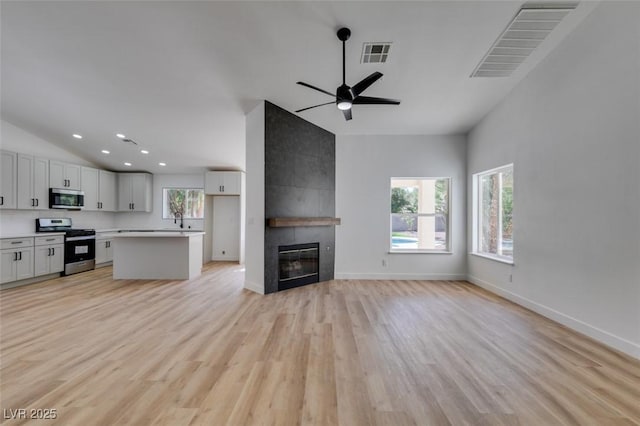 6126 Bedrock Ct, North Las Vegas, NV 89031 - unfurnished living room featuring lofted ceiling, healthy amount of natural light, light wood-type flooring, ceiling fan, and a tiled fireplace