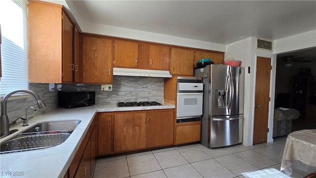 5209 Del Monte Ave, Las Vegas, NV 89146 - kitchen with appliances with stainless steel finishes, under cabinet range hood, brown cabinetry, and tasteful backsplash