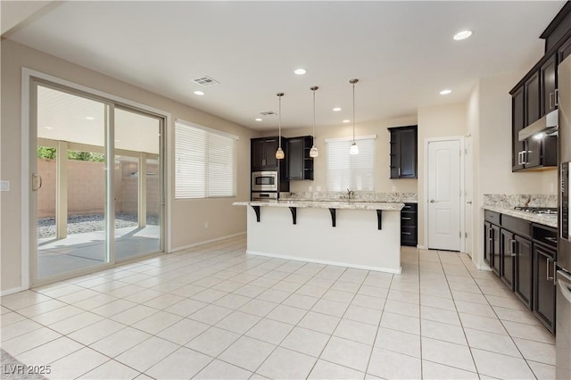 1633 Dornie Ave, North Las Vegas, NV 89084 - kitchen featuring a kitchen bar, under cabinet range hood, a kitchen island, light stone counters, and appliances with stainless steel finishes