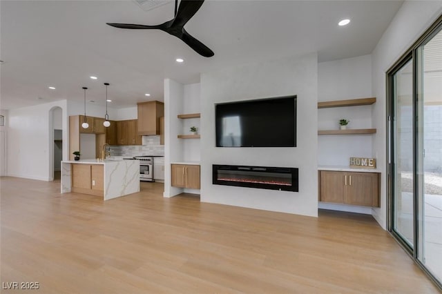 10452 Niagara Falls Ln, Las Vegas, NV 89144 - unfurnished living room with a ceiling fan, light wood-style flooring, a glass covered fireplace, recessed lighting, and built in shelves