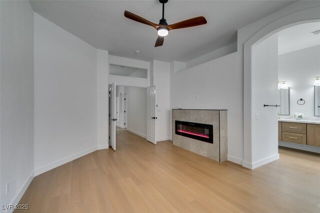 10452 Niagara Falls Ln, Las Vegas, NV 89144 - unfurnished living room with light wood-style floors, ceiling fan, a glass covered fireplace, and arched walkways