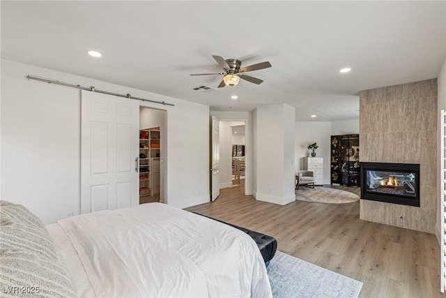 712 Proud Eagle Ln, Las Vegas, NV 89144 - bedroom with light wood-style flooring, recessed lighting, a barn door, a spacious closet, and a tile fireplace