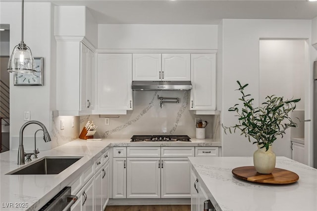 712 Proud Eagle Ln, Las Vegas, NV 89144 - kitchen with stainless steel appliances, under cabinet range hood, white cabinetry, light stone countertops, and decorative light fixtures