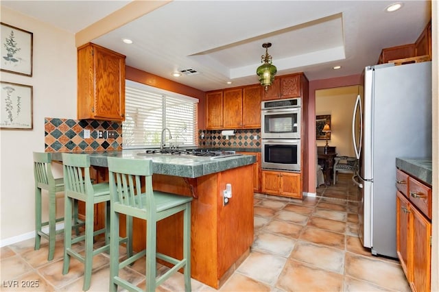 8875 Tidal Bay Dr, Las Vegas, NV 89117 - kitchen featuring appliances with stainless steel finishes, a tray ceiling, brown cabinetry, tasteful backsplash, and recessed lighting