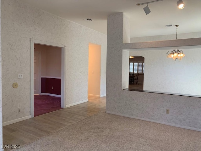 6704 Lost River Ct, Las Vegas, NV 89108 - carpeted empty room with a chandelier, arched walkways, wood finished floors, and wallpapered walls