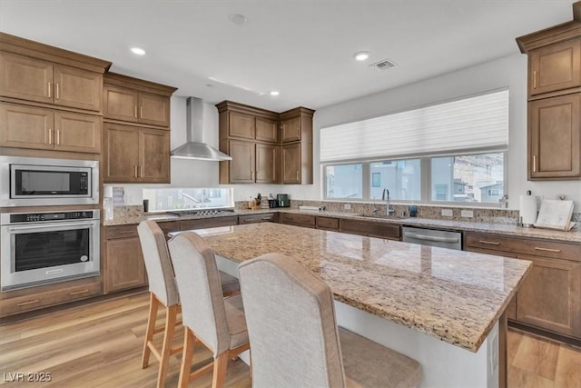11695 Gentle Birdsong Ave, Las Vegas, NV 89138 - kitchen featuring appliances with stainless steel finishes, wall chimney exhaust hood, a kitchen island, light wood-type flooring, and recessed lighting