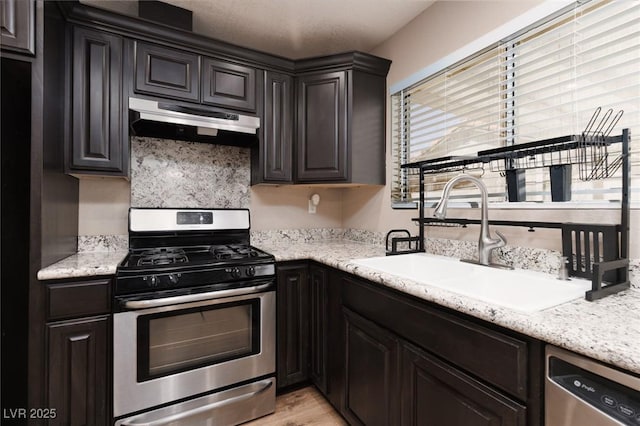 317 Brent Ct, Henderson, NV 89074 - kitchen featuring appliances with stainless steel finishes, under cabinet range hood, light wood-type flooring, light stone counters, and tasteful backsplash