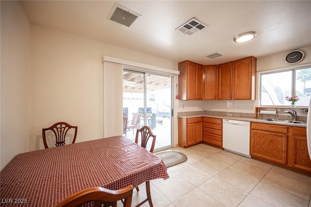 4616 E Idaho Ave, Las Vegas, NV 89104 - kitchen featuring white dishwasher, light countertops, brown cabinetry, light tile patterned flooring, and backsplash