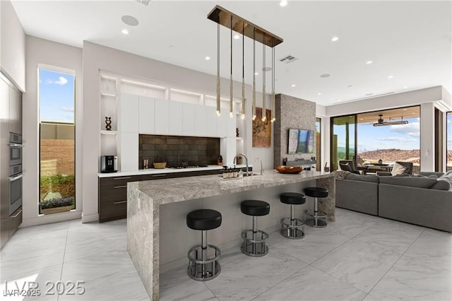 387 Solitude Peak Ln, Henderson, NV 89012 - kitchen featuring light marble finish floors, modern cabinets, a kitchen breakfast bar, open floor plan, and black stovetop