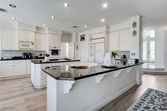 2496 Ram Crossing Way, Henderson, NV 89074 - kitchen with white appliances, a breakfast bar, light wood-type flooring, decorative backsplash, and a peninsula