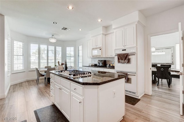 2496 Ram Crossing Way, Henderson, NV 89074 - kitchen with white appliances, a kitchen island, tasteful backsplash, white cabinets, and light wood-style flooring