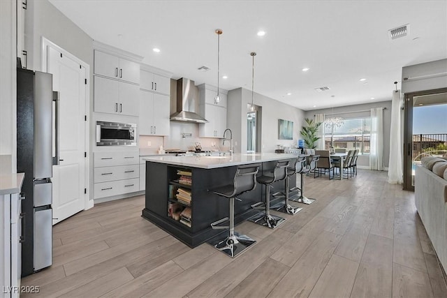 112 Springbough Ln, Las Vegas, NV 89138 - kitchen featuring wall chimney range hood, appliances with stainless steel finishes, light countertops, light wood-style floors, and a breakfast bar