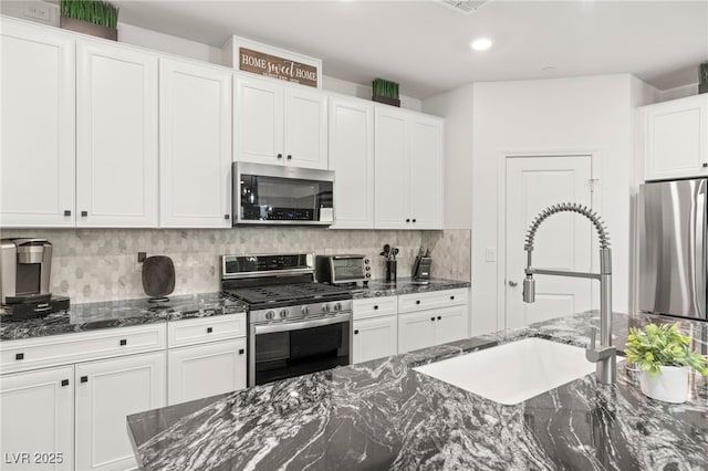 2833 Sangro Ct, Henderson, NV 89044 - kitchen with stainless steel appliances, tasteful backsplash, white cabinets, dark stone countertops, and recessed lighting