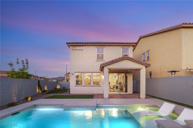 2833 Sangro Ct, Henderson, NV 89044 - back of house at dusk featuring a tiled roof, stucco siding, a fenced backyard, and a patio area