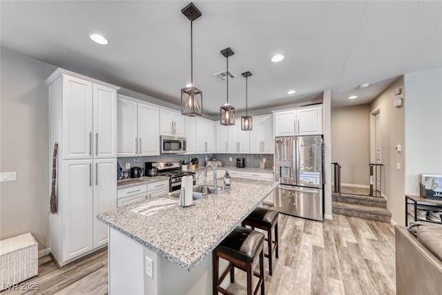 6335 Pacific Sky St, North Las Vegas, NV 89081 - kitchen featuring appliances with stainless steel finishes, light wood-type flooring, white cabinetry, tasteful backsplash, and a breakfast bar