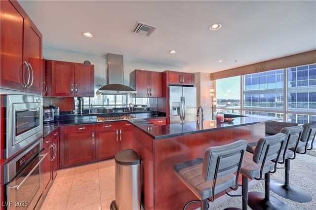 4575 Dean Martin Dr Unit 1112, Las Vegas, NV 89103 - kitchen featuring stainless steel appliances, wall chimney exhaust hood, dark countertops, an island with sink, and a breakfast bar area