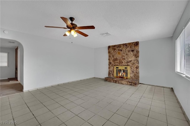 75 N 27th St, Las Vegas, NV 89101 - unfurnished living room featuring a ceiling fan, a fireplace, arched walkways, a textured ceiling, and light tile patterned floors