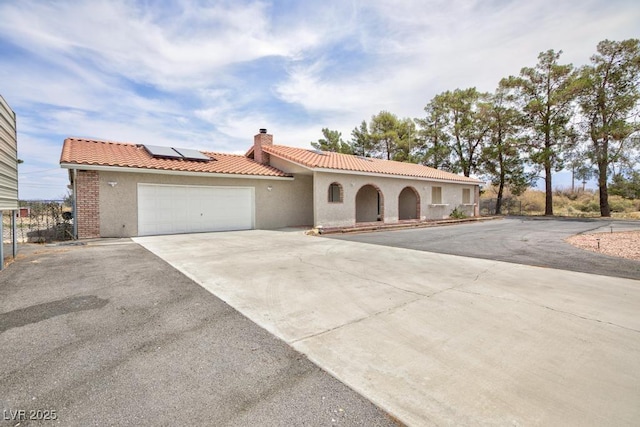 1050 Morgan Ln, Pahrump, NV 89060 - mediterranean / spanish home featuring driveway, a tiled roof, roof mounted solar panels, a garage, and a chimney