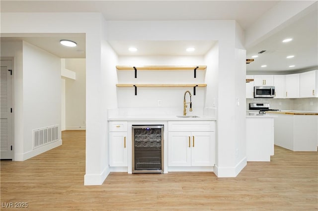 2107 Fountain Springs Dr, Henderson, NV 89074 - indoor wet bar featuring beverage cooler, stainless steel microwave, stove, light wood finished floors, and recessed lighting