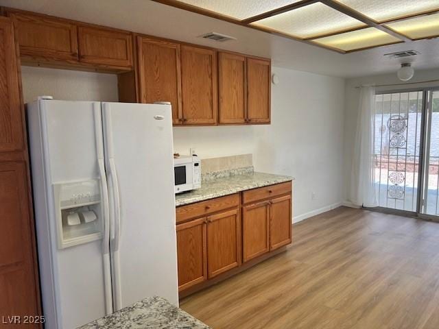 9600 Pacific View Dr, Las Vegas, NV 89117 - kitchen featuring white appliances, brown cabinetry, light wood finished floors, and light stone countertops