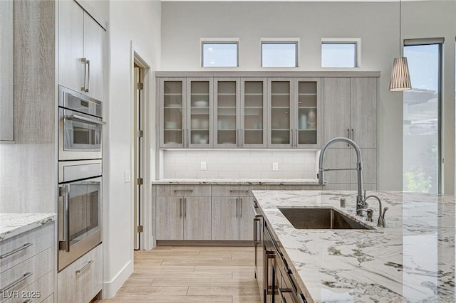33 Hassayampa Trl, Henderson, NV 89052 - kitchen featuring decorative backsplash, glass insert cabinets, light stone counters, light wood-type flooring, and decorative light fixtures