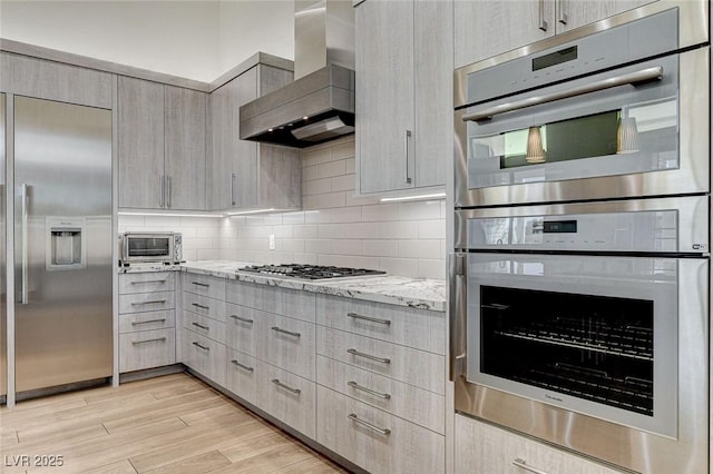 33 Hassayampa Trl, Henderson, NV 89052 - kitchen featuring wall chimney exhaust hood, stainless steel appliances, light stone countertops, light wood-style flooring, and modern cabinets