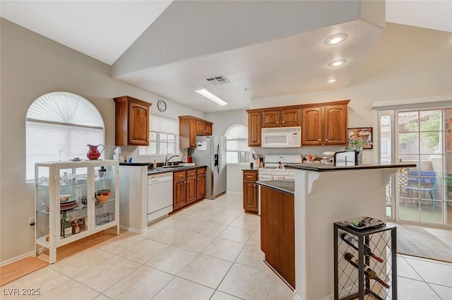 2925 Wigwam Pkwy Unit 123, Henderson, NV 89074 - kitchen featuring white appliances, dark countertops, light tile patterned floors, brown cabinetry, and a breakfast bar area