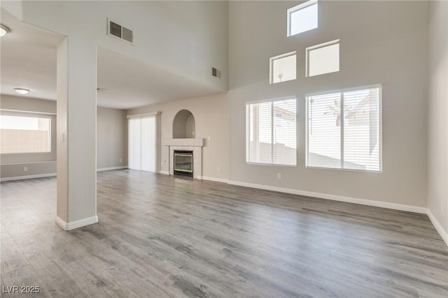 7816 Calico Flower Ave, Las Vegas, NV 89128 - unfurnished living room featuring wood finished floors, healthy amount of natural light, a tiled fireplace, and a high ceiling