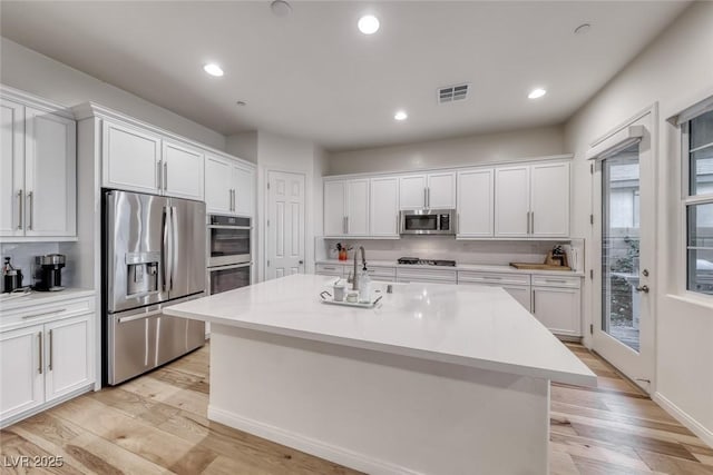32 Tatahatso Point St, Henderson, NV 89011 - kitchen with stainless steel appliances, white cabinetry, light countertops, light wood-style flooring, and an island with sink