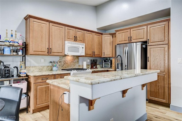8926 Termoli St, Las Vegas, NV 89123 - kitchen with white microwave, light wood-style floors, stainless steel refrigerator with ice dispenser, light stone countertops, and a towering ceiling