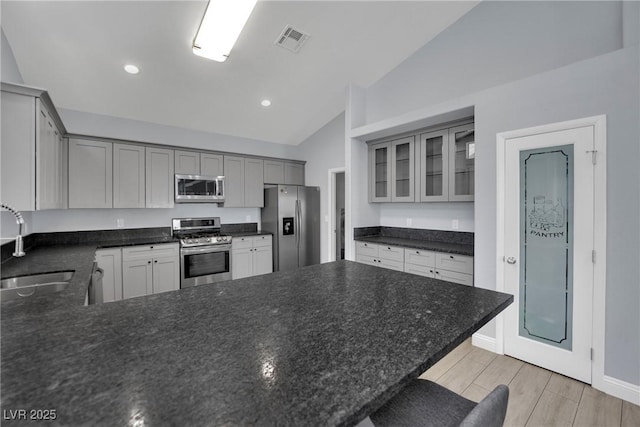 5509 Rose Thicket St, Las Vegas, NV 89130 - kitchen with appliances with stainless steel finishes, vaulted ceiling, a peninsula, glass insert cabinets, and gray cabinetry