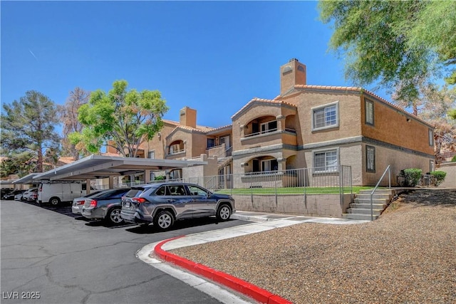 201 Mission Laguna Ln Unit 104, Las Vegas, NV 89107 - view of front facade featuring covered and uncovered parking, a chimney, a tile roof, and stucco siding