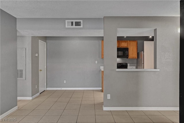 201 Mission Laguna Ln Unit 104, Las Vegas, NV 89107 - kitchen with black microwave, stove, brown cabinets, light tile patterned floors, and freestanding refrigerator