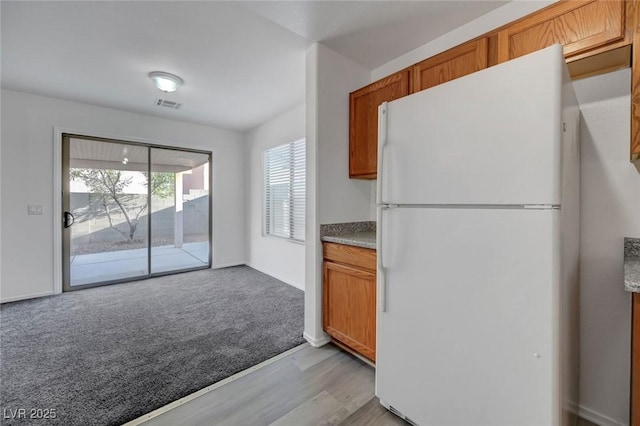 4751 Lone Grove Dr, Las Vegas, NV 89139 - kitchen featuring freestanding refrigerator, light wood-style flooring, brown cabinetry, light colored carpet, and light countertops
