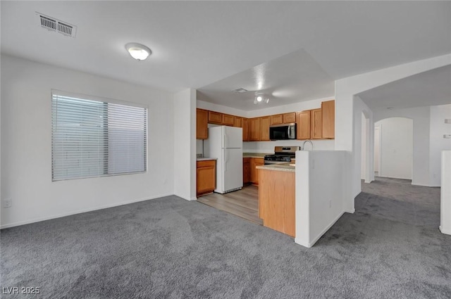 4751 Lone Grove Dr, Las Vegas, NV 89139 - kitchen with black microwave, freestanding refrigerator, stainless steel range, carpet floors, and arched walkways