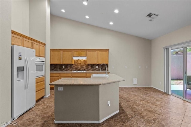 9233 Onyx Point Ct, Henderson, NV 89074 - kitchen featuring white appliances, under cabinet range hood, tasteful backsplash, an island with sink, and light countertops