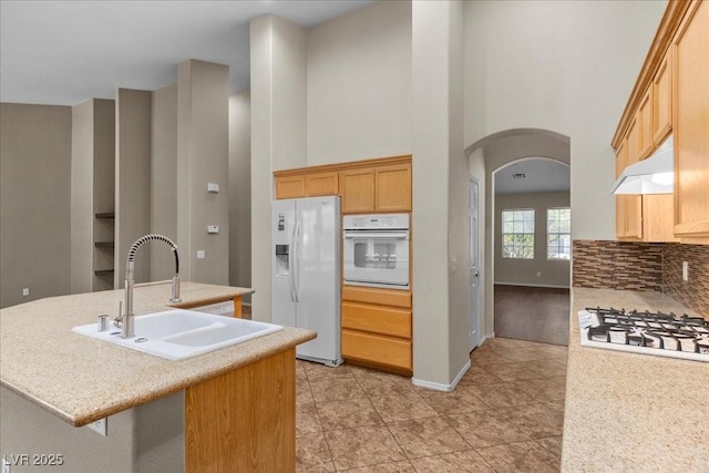 9233 Onyx Point Ct, Henderson, NV 89074 - kitchen featuring white appliances, arched walkways, under cabinet range hood, a high ceiling, and tasteful backsplash
