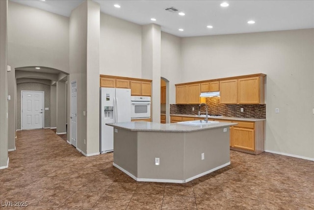 9233 Onyx Point Ct, Henderson, NV 89074 - kitchen featuring arched walkways, white appliances, a towering ceiling, a center island with sink, and tasteful backsplash